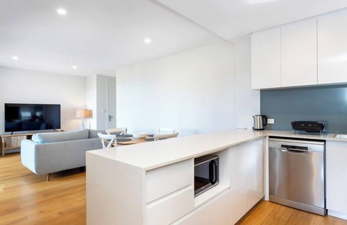 Leederville Apartment | Rooftop Sky Lounge has a daybed, tables and stools, a lounge area with a big screen TV and a grassed